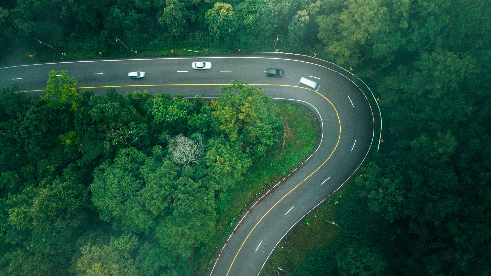 Vista aérea de uma estrada sinuosa rodeada por floresta, com veículos em circulação.