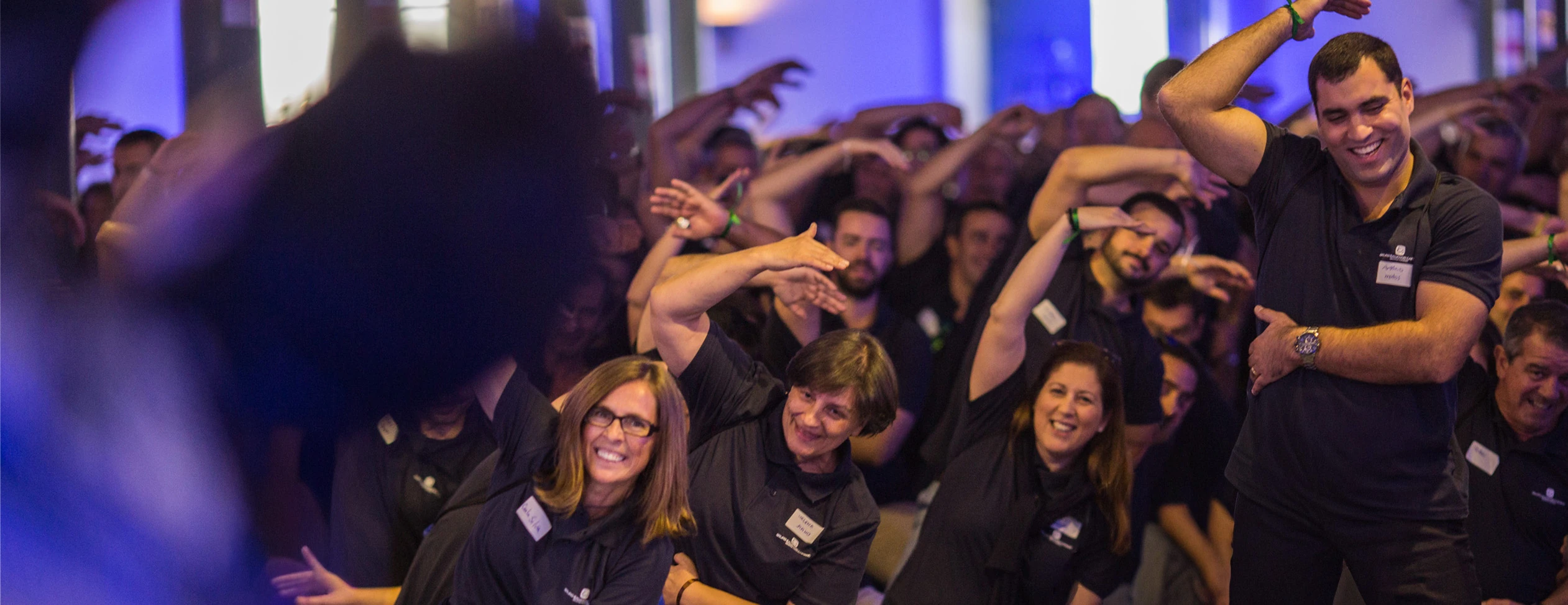 Grupo de colaboradores reunidas num espaço interior, em ambiente de evento corporativo.