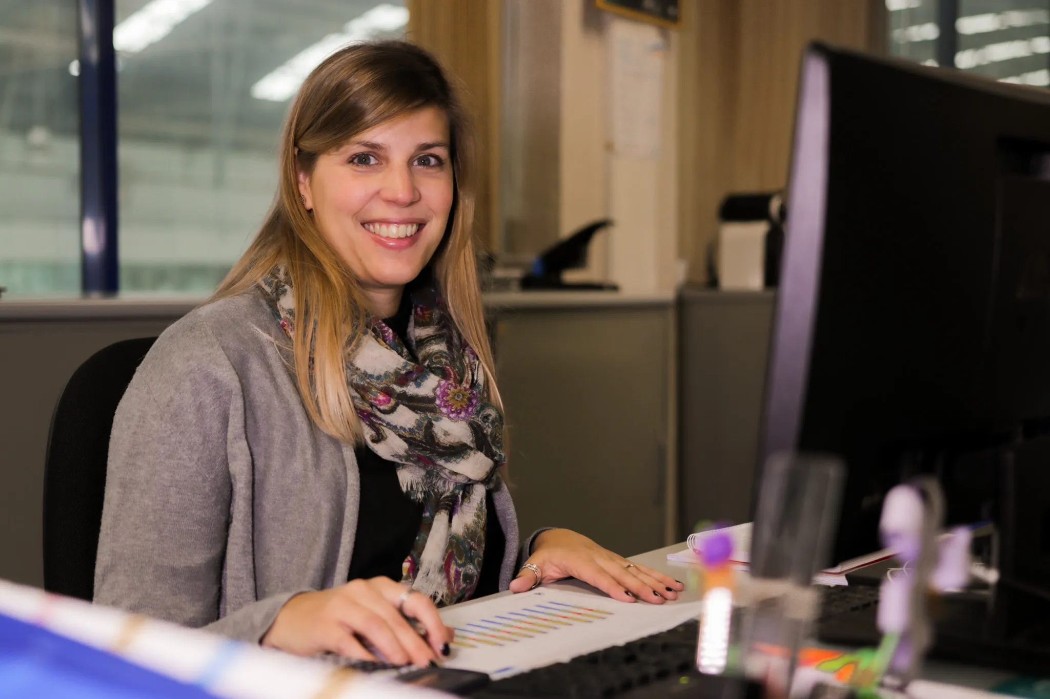 Colaboradora a trabalhar num escritório, sentada à secretária com computador, em ambiente profissional.