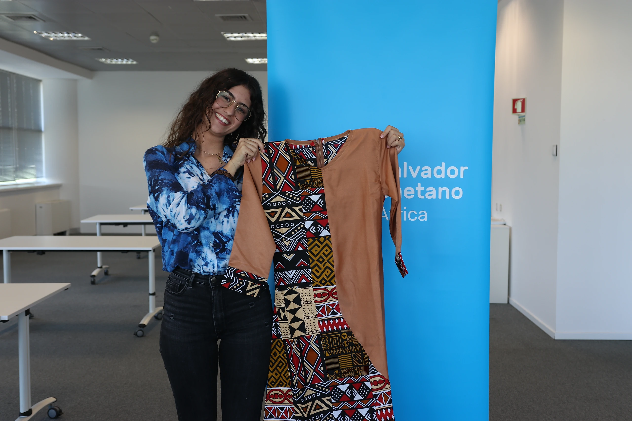 Colaboradora num espaço corporativo a interagir junto a um elemento expositivo, mostrando um vestido de África.