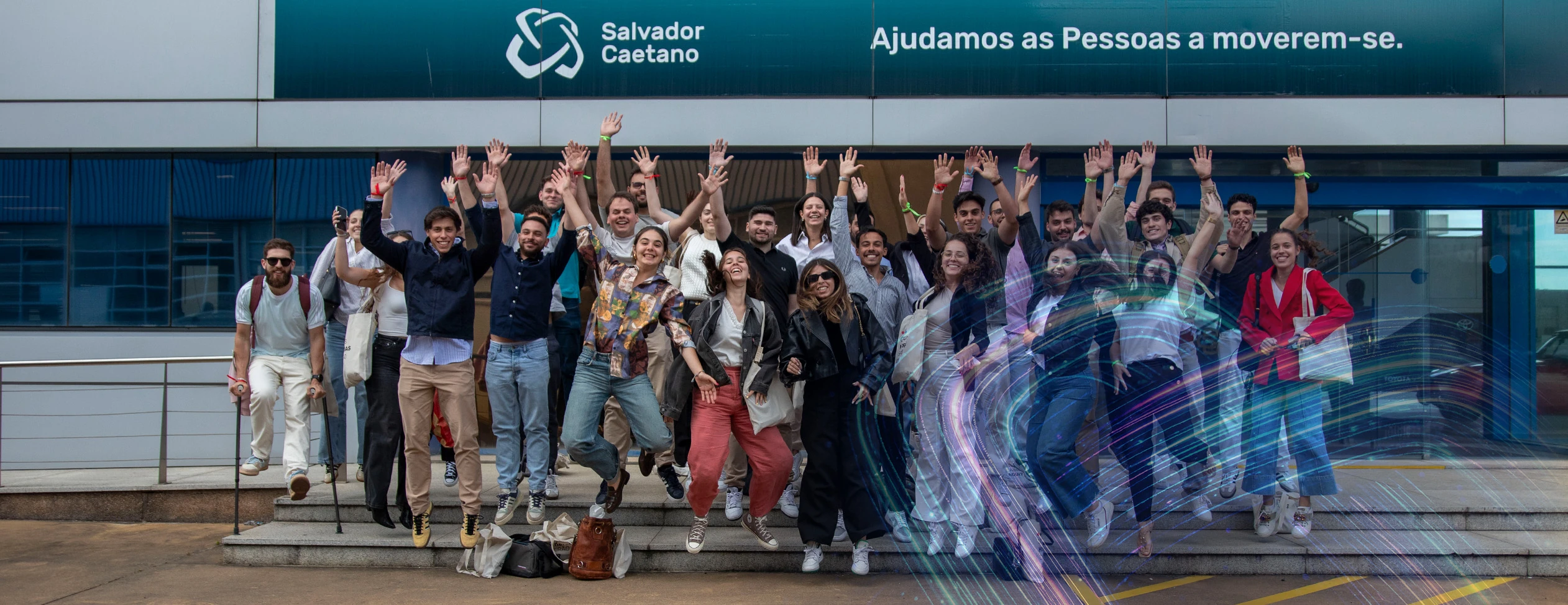 Grupo de jovens reunidos em frente ao edifício sede do Grupo, com braços erguidos, em contexto de evento institucional.