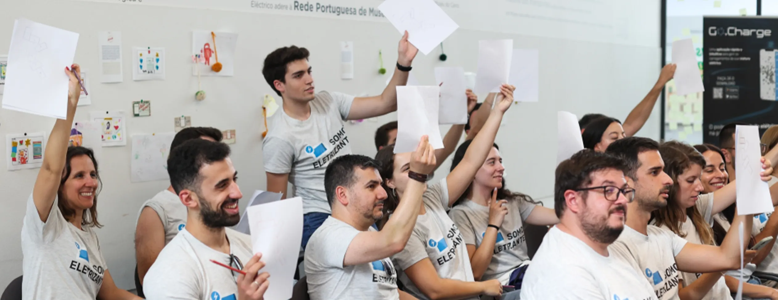 Colaboradores em reunião de trabalho à mesa, com folhas nas mãos num ambiente profissional.
