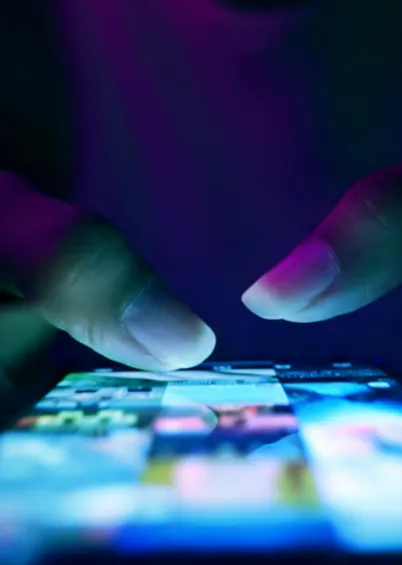 Uma visão em close-up de duas pontas de dedos a interagir com o ecrã de um smartphone que exibe miniaturas coloridas.