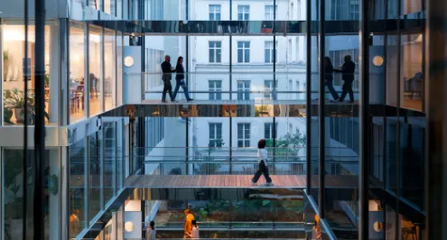 Pessoas a caminhar em passarelas de vidro num edifício de escritórios moderno e com vários andares.