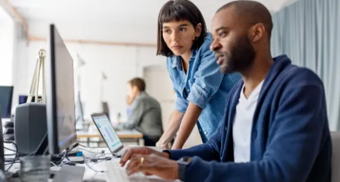 Um homem e uma mulher a trabalhar juntos num computador, com o homem a digitar e a mulher a observar o ecrã