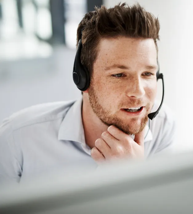 Retrato de um homem com fones de ouvido e microfone, sorrindo e olhando para um monitor de computador.
