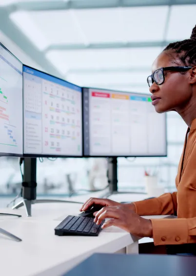 Uma mulher a usar óculos e a trabalhar num computador com dois ecrãs, mostrando vários gráficos e dados.