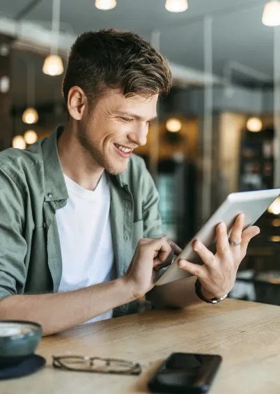 Um homem sorridente de camisa verde sentado numa mesa de café a usar um tablet.