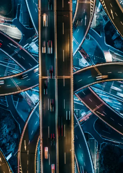 Vista aérea de um cruzamento de autoestrada movimentado durante a noite, com os rastos de luzes dos carros em movimento.