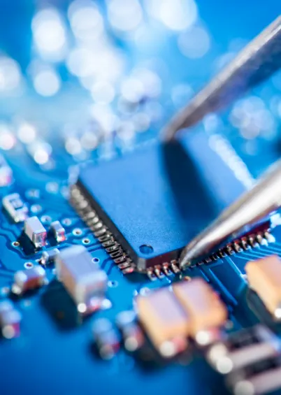 Uma vista em close-up de um chip azul numa placa de circuito, com uma pinça a tocar num dos pinos.